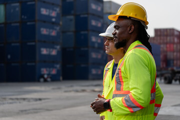 Industrial engineer standing at shipping container yard inspecting cargo delivering loading as plan. Cargo manager and diverse ethnic worker checking import export container at logistic terminal dock.