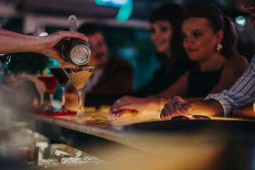 Naklejka premium A bartender skillfully pours cocktails for a group of friends enjoying a night out at a vibrant bar, creating a lively and social atmosphere.