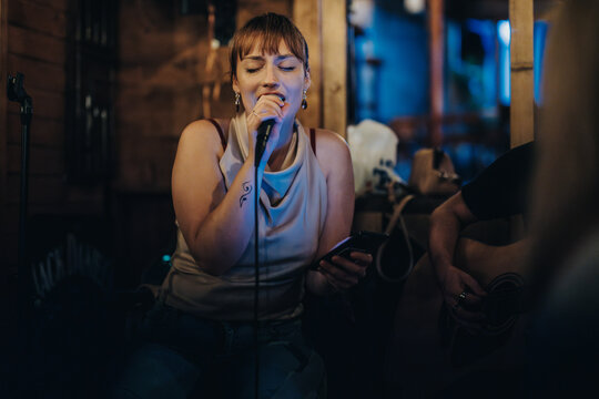 A woman sings passionately in a warm, dimly-lit venue, showcasing emotion and engagement with her music in a live performance setting.
