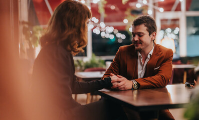 A couple shares a romantic moment at a cozy restaurant, holding hands and smiling warmly. The intimate ambiance is enhanced by decorative lighting and a comfortable setting.