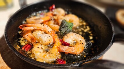 Classic Spanish dish —Gambas al ajillo (Garlic Shrimp) in Olive Oil (Gambas al Ajillo) with sliced ​​olive sourdough bread, served hot in a cast iron pan at a bistro bar or restaurant