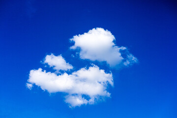 A bright blue sky with three white clouds floating in the center. The clouds have a fluffy texture and range in color from dark blue to bright blue. This image gives a sense of peace and beauty.