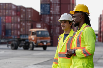 Industrial engineer standing at shipping container yard inspecting cargo delivering loading as plan. Cargo manager and diverse ethnic worker checking import export container at logistic terminal dock.