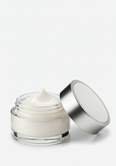 Open glass jar filled with white cream and metal lid on white background