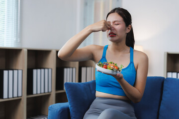 Young woman disgusted by smell of her salad while sitting on sofa at home