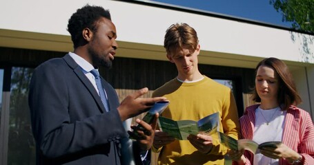 A realtor shows advertising bills to customers standing outside the house on a summer day