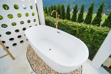 Phetchabun, Thailand - June, 06, 2025 :Outdoor freestanding bathtub surrounded by lush greenery and pebbles with mountain view in the background at Phetchabun, Thailand