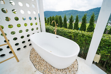 Phetchabun, Thailand - June, 06, 2025 :Outdoor freestanding bathtub surrounded by lush greenery and pebbles with mountain view in the background at Phetchabun, Thailand