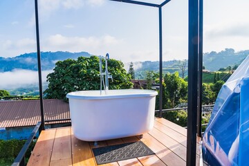 Phetchabun, Thailand - June, 06, 2025 :Outdoor freestanding bathtub surrounded by lush greenery and pebbles with mountain view in the background at Phetchabun, Thailand