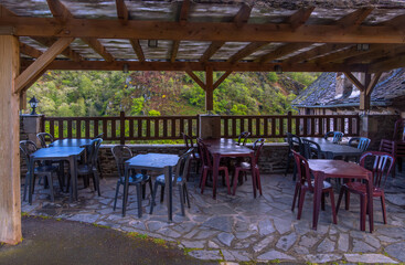 An open-air mountain restaurant terrace with empty plastic tables and chairs in a rural setting overlooking a green landscape.