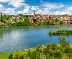 Panoramic view of the houses, historic architecture, and church of Albi, France, from the green Tarn River with a young couple in love having a picnic on the riverbank.