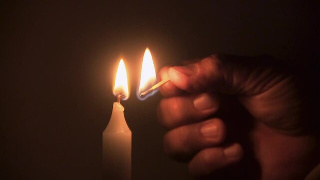 Close-up of male hands lighting a candle with matches, flame burning steadily in calm indoor setting