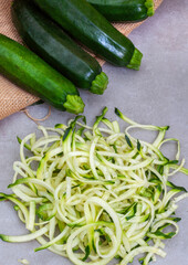 Pile of grated zucchini is on a table next to some green zucchini