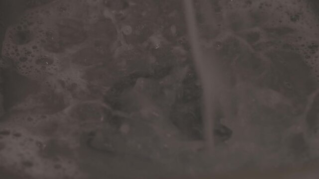 Close-up shot of soapy water flowing down a kitchen sink as hands wash dishes