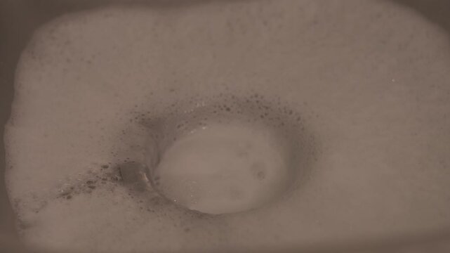 Close-up shot of soapy water running down the sink as a person washes dishes, capturing a common household cleaning task.