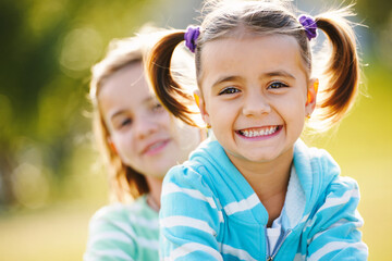 Happy young girls smile outdoors on a sunny day, backlighting creates a golden glow around their hair.