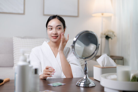 Young asian woman applying cream on face at home - Powered by Adobe