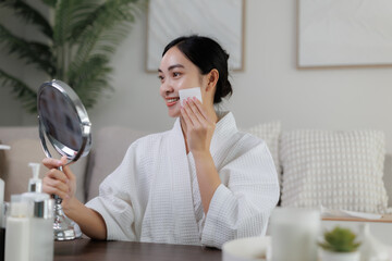 Smiling woman applying makeup with cotton pad and holding mirror