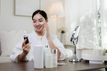 Smiling woman applying moisturizer on face at home