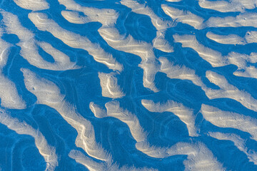 Troughs in the sand caused by receding seawater create deep shadows.