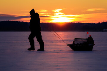Silhouette of Man with Sled Walking on Frozen Forest Lake at Sunrise
