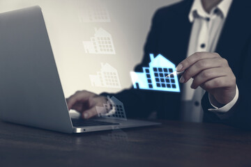 Real estate agent touching house icon on virtual screen while working on laptop at table, closeup....