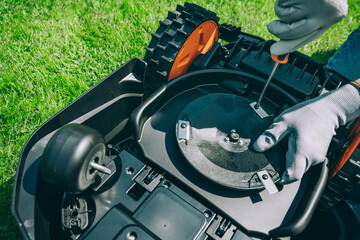 A man changes the blades of a robotic lawn mower. Lawn Mower Maintenance at Home Workshop With...