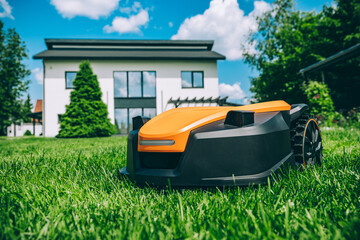 Automatic robotic lawn mower on a green lawn with modern house in background. Grass lawn mower...