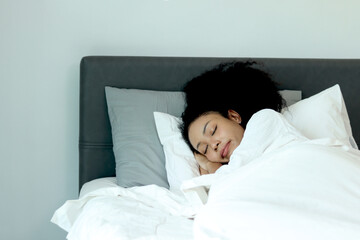 Beautiful woman with curly hair sleeping on comfortable bed at the bedroom. African female sleeping...