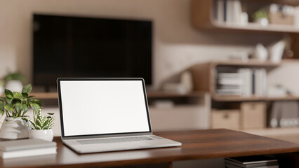 White screen laptop and potted plants on wooden table in a cosy living room with TV and bookshelf.