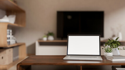 Blank screen laptop and books with potted plants aside on wooden table in a living room or bedroom.