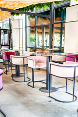 Modern cafe interior with pastel velvet chairs, marble tables, and large windows. The ceiling features greenery and geometric decor, creating a cozy and elegant atmosphere.