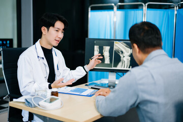 Asian doctor discusses knee X-ray results with senior patient in modern clinic. Concept of orthopedic consultation, bone care, health diagnosis