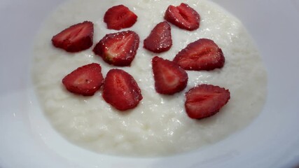 Porridge with pieces of ripe strawberry. Oats gruel top view. Cutting with knife strawberry in 2 parts, white plate 4k. - Powered by Adobe