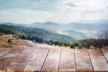 A weathered wooden table set against a breathtaking blurred mountain landscape invites thoughts of outdoor serenity, travel, and rustic adventure