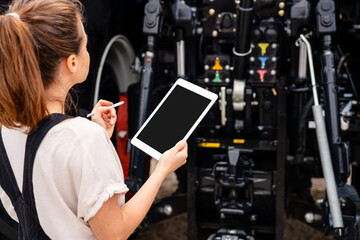Woman technician inspecting tractor with digital tablet at farm equipment site