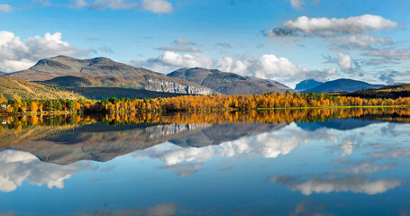 beautiful scenic landscape with mountain and autumnal forest under the sky reflecting in surface of water in Norway.