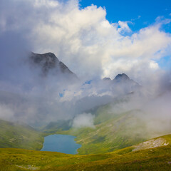 small lake in green mountain valley bowl in dense mist and clouds