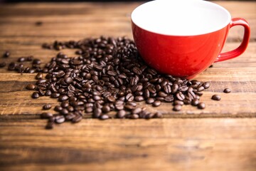 Flat design red ceramic mug is sitting on wooden tabletop with scattered coffee beans in foreground