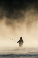 Fisherman Fly Fishing on Misty River During Early Morning Light