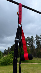 Close-up of TRX suspension training straps hanging on outdoor workout equipment under cloudy sky – calisthenics and fitness concept