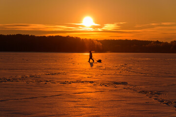 Panoramic Winter View of a Frozen Forest Lake with a Fisherman Walking Toward the Sunrise	