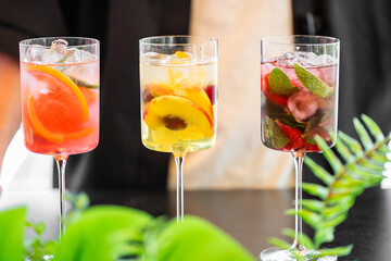 Three glasses of colorful cocktails with ice cubes, garnished with citrus slices, berries, and mint...