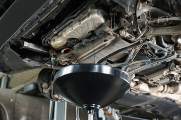 Dirty old motor oil dripping from car engine into container in workshop, closeup