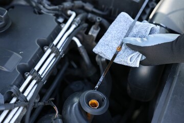 Worker checking motor oil level in car with dipstick, closeup