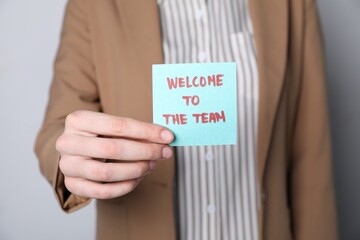 Human resources manager holding sticky note with word Welcome To The Team on grey background,...