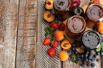 Different jams in jars and ingredients on wooden table, flat lay. Space for text