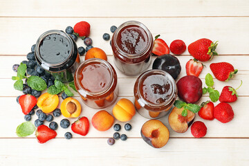 Different jams in jars and ingredients on white wooden table, flat lay