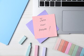 Paper note with phrase Join Our Team, laptop and stationery on white wooden table, flat lay