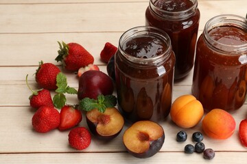 Different jams in jars and ingredients on white wooden table